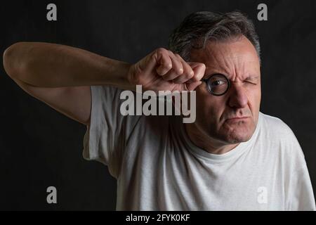 Ein Mann hält eine Lupe vor sich Auge schaut durch sie mit einem sehr lustigen Ausdruck Stockfoto