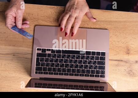 Ältere Ehepartner, Männer und Frauen, in der Nähe eines offenen Laptop-Monitors. Beschnittenes Foto von Mann Hand mit Kreditkarte und Frau Hand arbeiten beim Tippen Stockfoto