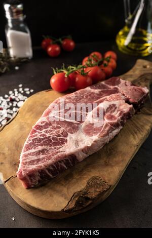 Selektiver Fokus. Rohes Steak aus marmortiertem Schweinefleisch im rustikalen Stil. Vor dem Kochen. Auf einem Holzbrett, mit grobem Salz und Gewürzen. Low-Key, Nahaufnahme Stockfoto