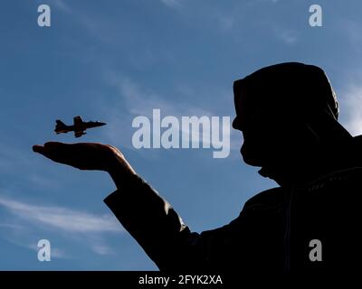 Silhouette eines Kapuzenmannes, der ein Flugzeug fliegen hat Über seine offene Hand gegen einen schönen blauen Himmel Stockfoto