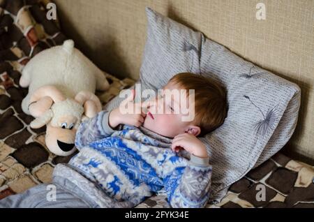 Ein 4-jähriger rothaariger Junge liegt auf dem Bett und pflückt sich mit dem Finger die Nase. Kind, das seine Nase pflückt Stockfoto