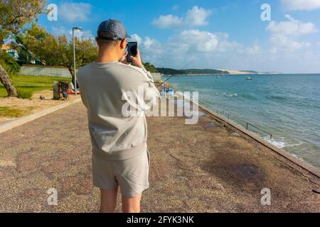 Arcachon, Frankreich, Touristen zu Besuch, Strandszenen, Urlaub, Mann, der Fotos mit Smartphone macht, hinten Stockfoto