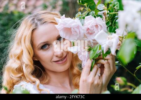 Frau riecht und genießt schöne Rosen Blumen schönen sonnigen Frühlingstag. Lächelnde junge Frau posiert mit Blütenblumen mit positiver Emotion. Weibliches Gesicht mit Blumen. Stockfoto