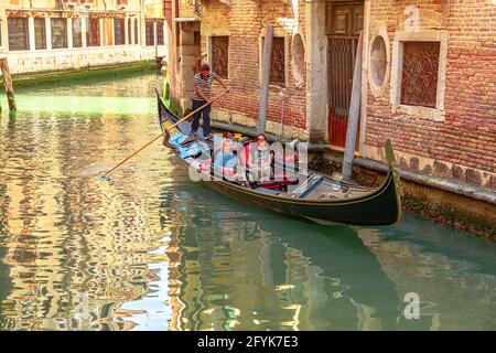 Venedig, Italien - 9. Mai 2021: Traditionelle Gondoliere in Venedig nehmen Touristen mit auf Tour auf dem historischen Canal Grande der Stadt. Menschen mit Maske für Stockfoto