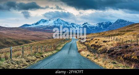 Die Straße hinunter in Richtung der schneebedeckten Cuillin Berge auf der Isle of Skye. Stockfoto