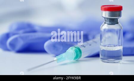 Glasampulle mit Impfstoff gegen Coronavirus, COVID-19, Influenza, Diabetes und andere Krankheiten undSpritze Auf dem Tisch vor dem Hintergrund der medizinischen Handschuhe Stockfoto