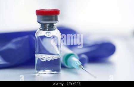 Glasampulle mit Impfstoff gegen Coronavirus, COVID-19, Influenza, Diabetes und andere Krankheiten undSpritze Auf dem Tisch vor dem Hintergrund der medizinischen Handschuhe Stockfoto