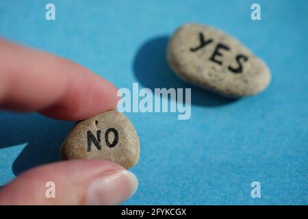 Die Hand wählt einen Stein mit dem Text No. Stone mit dem Wort Yes in Blur auf einem blauen Tisch. Auswahlkonzept. Stockfoto