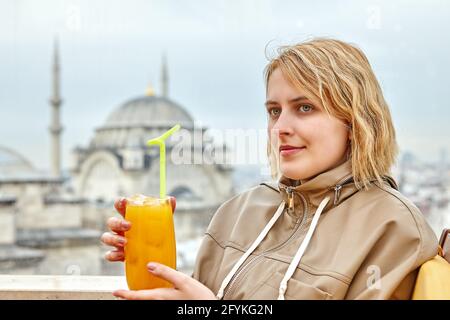 Junge Frau hält ein Glas Saft vor dem Fenster der Moschee. Stockfoto