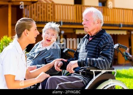 Senioren, paar Mann und Frau sitzen im Rollstuhl, Krankenschwester Hand in Hand mit Ihnen Stockfoto