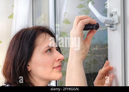 Reparatur des Griffs auf doppeltem Vinylfenster mit Moskitonetz. Junge Europäerin, die Schloss mit Schraubendreher fixiert. Stockfoto