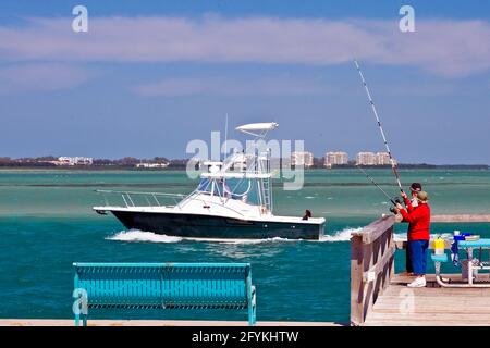 Älteres Paar, das vom Pier aus angeln kann, mit einer Yacht, die in der Nähe vorbeifährt, in der Nähe von, in der Nähe von, in der Nähe von, in der Nähe von, in der Stockfoto