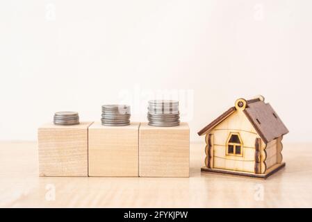 Modell des Hauses mit Münzstapeln auf Holzblöcken Auf beigefarbenem Tisch Stockfoto