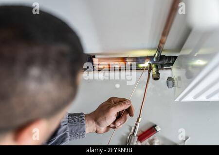 Unbekannter Industriearbeiter Klempner mit Zentralheizung Kupferrohre Schweißen Verwendung von Gasbrenner oder Lötlampe an der Wand im Haus Gebäude oder Wohnung - Stockfoto