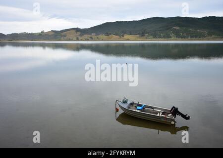 Kleines offenes Motorboot aus Metall mit schwarzem Außenbordmotor und Kabelführung, das in einem absolut ruhigen, geschlossenen Hafen festgemacht ist. Stockfoto