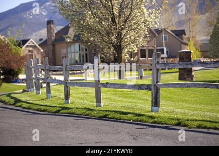 Holzzaun im Stil einer Ranch, der ein grünes Feld auf dem Land umgibt Stockfoto