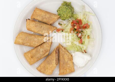 Blick von oben auf leckere Beilage von frittierten Chicken-Taquitos, die einzeln gerollt und in Stücke auf einem Teller geschnitten wurden. Stockfoto