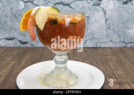 Garnelencocktail mit in Scheiben geschnittenen Gurken und Zitrusfrüchten, serviert in großem Becher in würziger roter Sauce als Vorspeise. Stockfoto