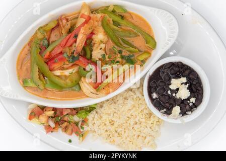 Blick von oben auf Garnelen, die in grüner Ranchero-Sauce gekocht und mit Reis und schwarzen Bohnen auf einem Teller serviert wurden. Stockfoto