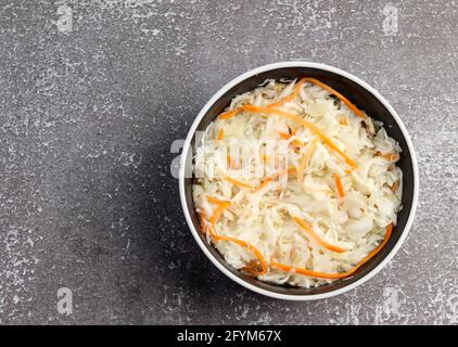 Hausgemachtes Sauerkraut mit Karotte in einer Schüssel auf dunklem Grund. Vegane Küche. Draufsicht, flach liegend Stockfoto