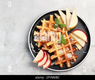 Wiener Waffeln serviert mit Früchten auf einem runden Teller auf hellgrauem Hintergrund. Draufsicht, flach liegend Stockfoto