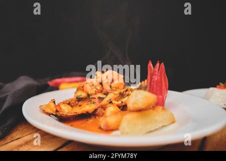 Peruanische Küche: Peruanische Gericht a lo Macho Fisch, Holztisch, serviert auf einem weißen Teller, (Fisch in Meeresfrüchtesauce gebraten, begleitet von Kartoffel Meer ​​bream a Stockfoto