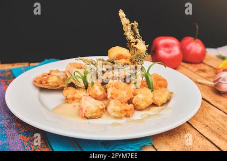 Peruanische Küche: Sautierte Garnelen mit Kräutern und Knoblauch, Holztisch, serviert auf einem weißen Teller, begleitet von purpurem Maissaft Stockfoto