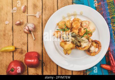 Peruanische Küche: Sautierte Garnelen mit Kräutern und Knoblauch, Holztisch, serviert auf einem weißen Teller, begleitet von purpurem Maissaft Stockfoto