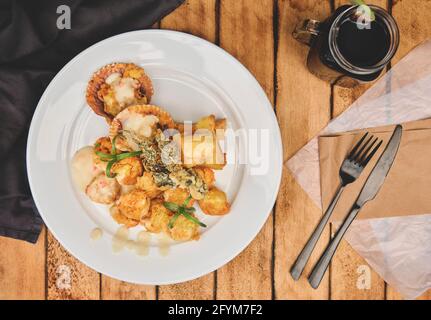 Peruanische Küche: Sautierte Garnelen mit Kräutern und Knoblauch, Holztisch, serviert auf einem weißen Teller, begleitet von purpurem Maissaft Stockfoto