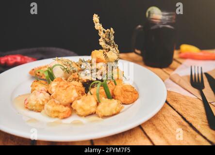 Peruanische Küche: Sautierte Garnelen mit Kräutern und Knoblauch, Holztisch, serviert auf einem weißen Teller, begleitet von purpurem Maissaft Stockfoto