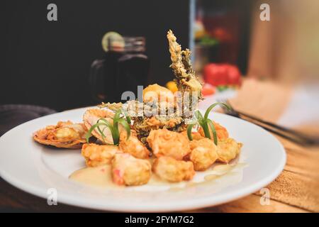 Peruanische Küche: Sautierte Garnelen mit Kräutern und Knoblauch, Holztisch, serviert auf einem weißen Teller, begleitet von purpurem Maissaft Stockfoto