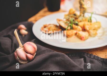 Peruanische Küche: Sautierte Garnelen mit Kräutern und Knoblauch, Holztisch, serviert auf einem weißen Teller, begleitet von purpurem Maissaft Stockfoto