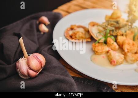 Peruanische Küche: Sautierte Garnelen mit Kräutern und Knoblauch, Holztisch, serviert auf einem weißen Teller, begleitet von purpurem Maissaft Stockfoto