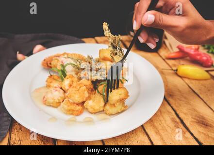 Peruanische Küche: Sautierte Garnelen mit Kräutern und Knoblauch, Holztisch, serviert auf einem weißen Teller, begleitet von purpurem Maissaft Stockfoto