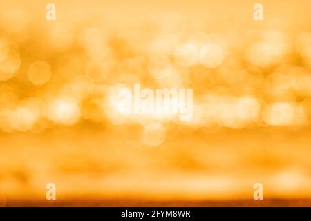 Abstrakte Natur Sommer oder Frühling Meer Meer Hintergrund. Kleine Wellen auf der goldenen, warmen Wasseroberfläche verwischen sich in Bewegung mit Bokeh-Lichtern vom Sonnenuntergang. Urlaub Stockfoto