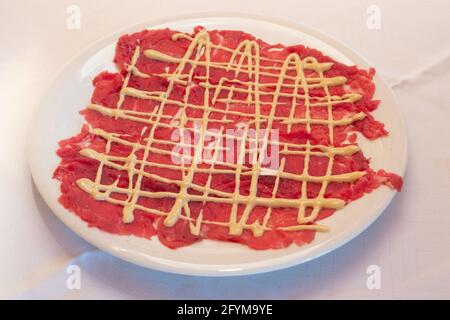 Carpaccio aus Rind mit Mayonnaise-Sauce im klassischen Cipriani-Stil Eine weiße Platte Stockfoto