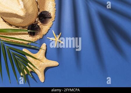 Palmblatt, Hut, Sonnenbrille und Seesterne auf blauem Hintergrund mit Kopierfläche. Stockfoto