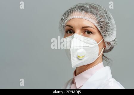 Porträt einer unglücklichen jungen Ärztin in einer medizinischen Maske auf grauem Hintergrund. Die müden Augen des Arztes. Das Konzept des Coronavirus. Stockfoto