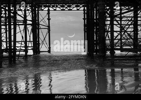 Halbmond durch einen Pier mit Reflexionen in der gesehen Nasser Sand Stockfoto