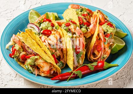 taco-Muscheln mit gegrillten Garnelen, Kohlsalat, Limette und Guacamole auf einem blauen Teller auf einem weißen Tisch, Nahaufnahme Stockfoto