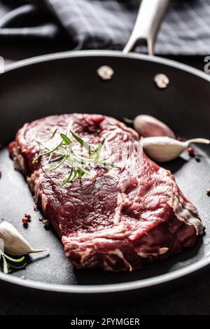 Frisches, rohes Rindfleisch Ribe Eye Steak in einer Teflonpfanne mit Rosmarin, Knoblauch, Salz und Pfeffer. Stockfoto