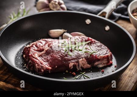 Frisches, rohes Rindfleisch Ribe Eye Steak in einer Teflonpfanne mit Rosmarin, Knoblauch, Salz und Pfeffer. Stockfoto