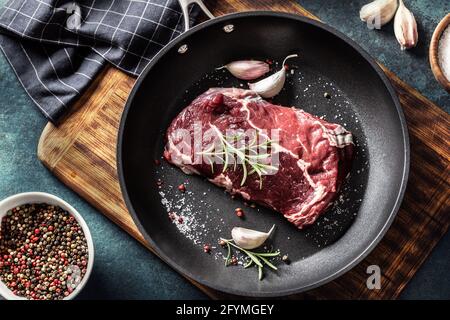 Frisches, rohes Rindfleisch Ribe Eye Steak in einer Teflonpfanne mit Rosmarin, Knoblauch, Salz und Pfeffer. Stockfoto