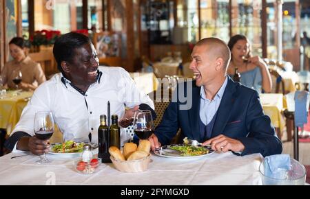 Zwei fröhliche männliche Freunde lächeln beim Abendessen in einem modischen Restaurant Stockfoto