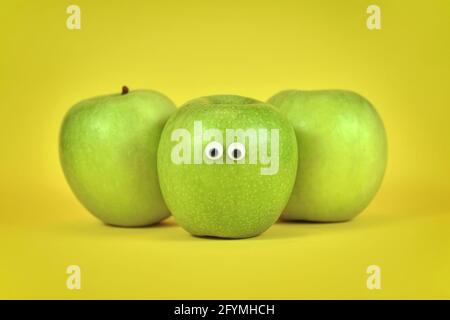 Grüne Apfelfrüchte mit lustigen schönen Augen auf hellem Gelb Hintergrund Stockfoto