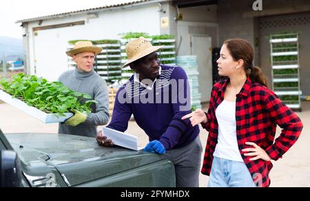 Mädchen Manager diskutieren mit Männern Arbeiter Lieferung von Setzlingen auf die Farm in einem Lager Stockfoto