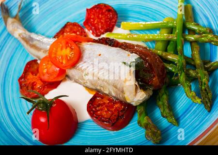 Blauer Wittling Fisch gebacken mit getrockneten Tomaten, Spargel und cremige Knoblauchsauce Stockfoto