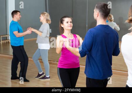 Gruppe glücklicher Erwachsener, die in der Tanzschule zu zweit moderne Gesellschaftstänze tanzen Stockfoto