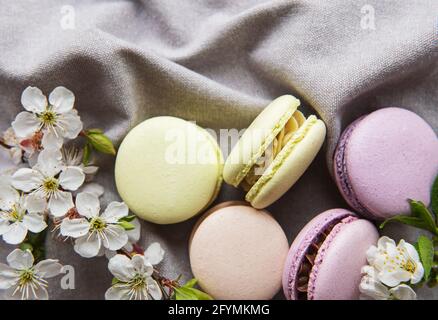 Französische süße Makronen bunte Vielfalt auf grauem Textilhintergrund Mit Frühlingsblüte Stockfoto