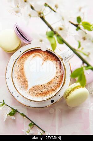 Kaffee mit herzförmigem Muster und süße Makronen-Desserts Ein rosa Kachelhintergrund Stockfoto